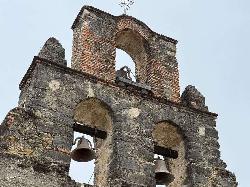 Old stone and brick bell tower with three bells at Mission Espada.