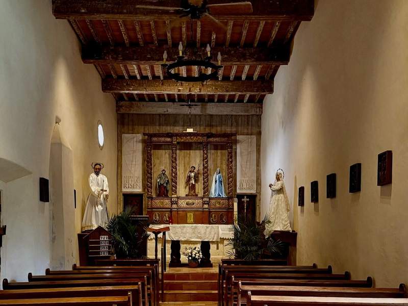 Mission church sanctuary with saint statues, wooden pews, and wooden ceiling.