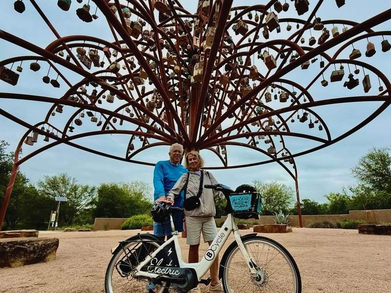 Two people with an e-bike beneath a large art installation with hanging art pieces