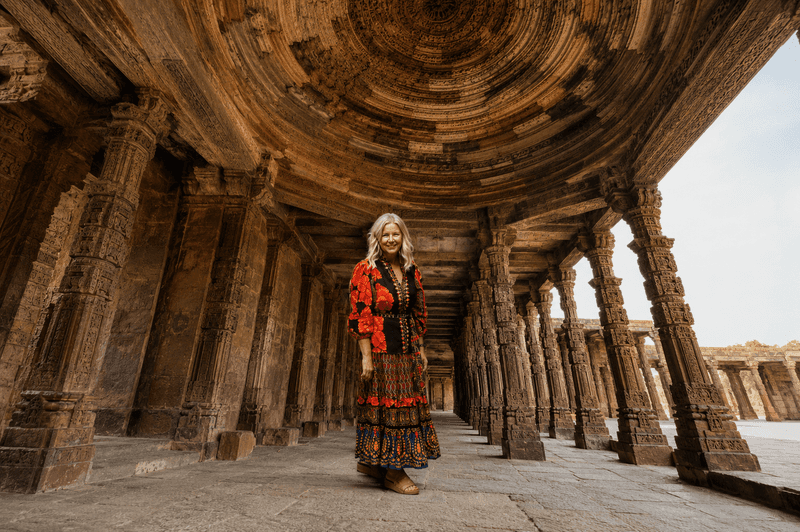 Woman standing beneath intricately carved stone arches in New Delhi, India.