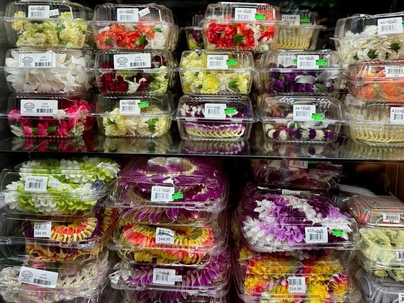 Colorful variety of leis in plastic containers stacked in a refrigerated case.