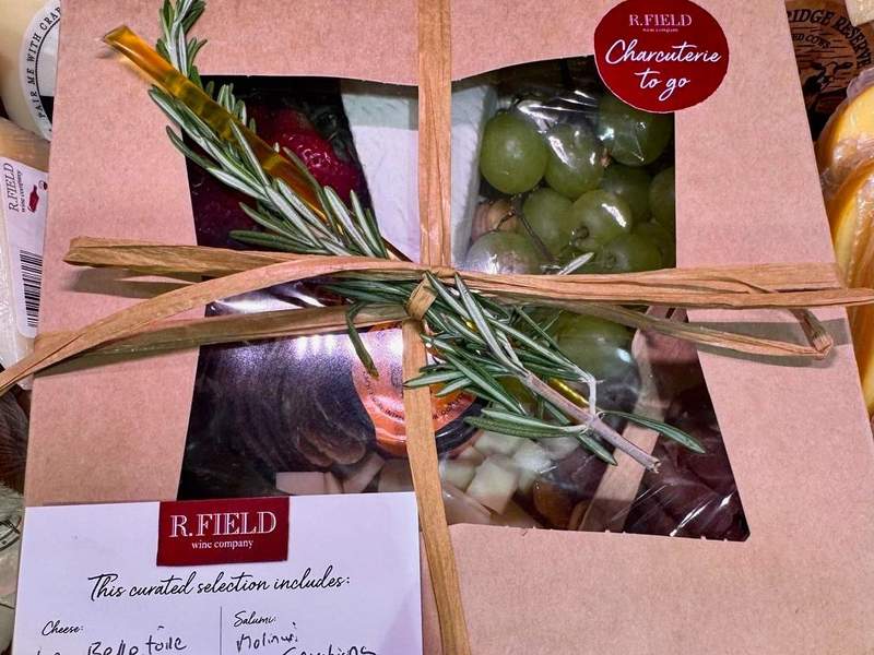 Charcuterie to go box that includes grapes cheese and sausage wrapped in a grass string.