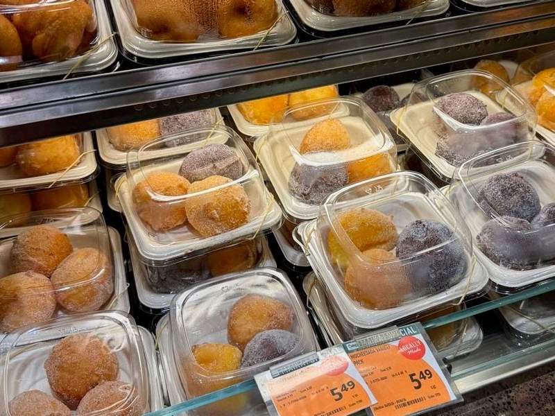 Homemade doughnuts and purple ube malasadas in plastic containers tagged with an orange deal tag.