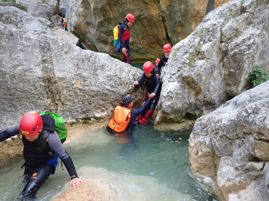 Guide assisting woman in wetsuit through canyong boulders into river in Aragon, Spain