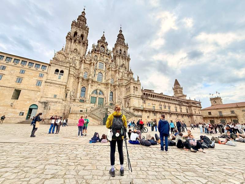 Pilgrims with backpacks resting and taking photos of the terminus of the Camino de Santiago the cathedral.