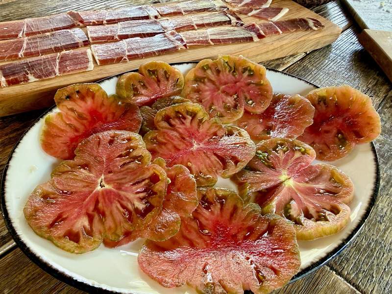 Giant sliced tomatoes and cured meats on plates.