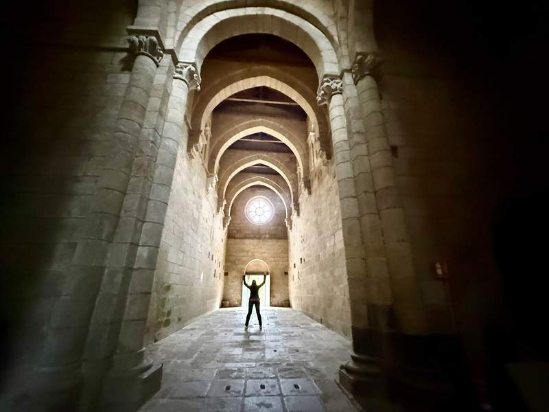 Looking down a stone corridor at a woman framed by light coming through an open door and circular window