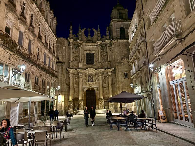 Couple walking down a beautiful city street framing an old church and lined with cafes.