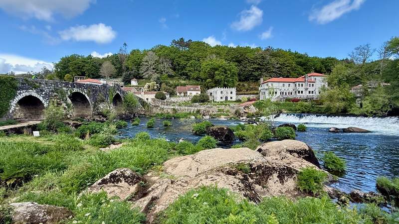 Looking over a river and Roman-style stone bridge at part of the village of Ponte Maceira.