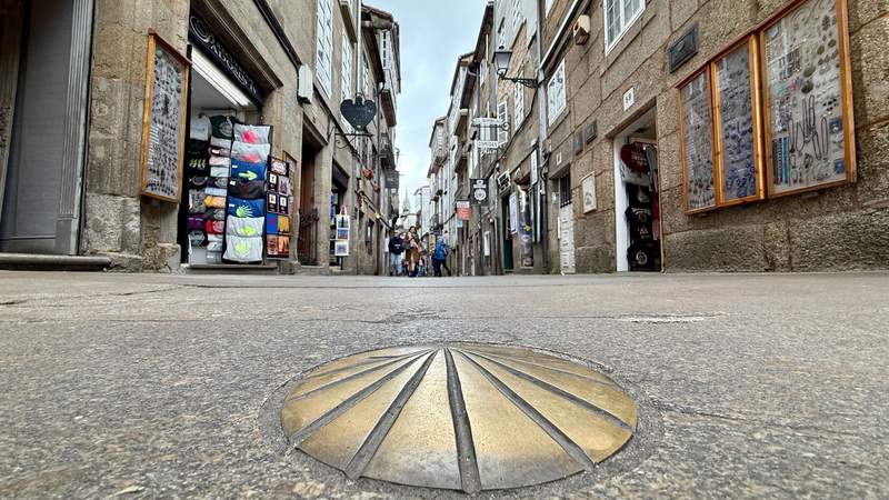 A bronze seashell set in the street of Santiago de Compostela, marking the way for the Camino de Santiago pilgrims with the Cathedral of Santiago de Compostela distantly in the background.