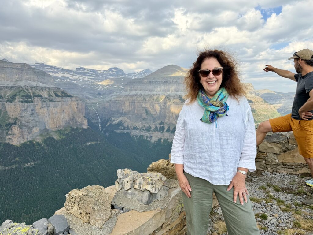 Woman wearing sunglasses with snow-capped peaks of the Spanish Pyrenees in the background.