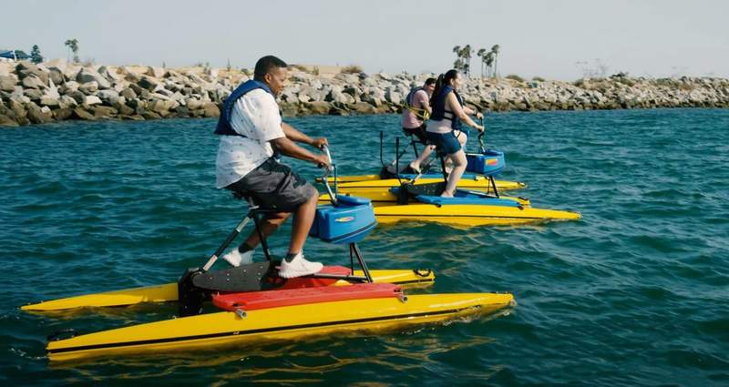 People driving a floating yellow hydrobike on the water in Long Beach. 