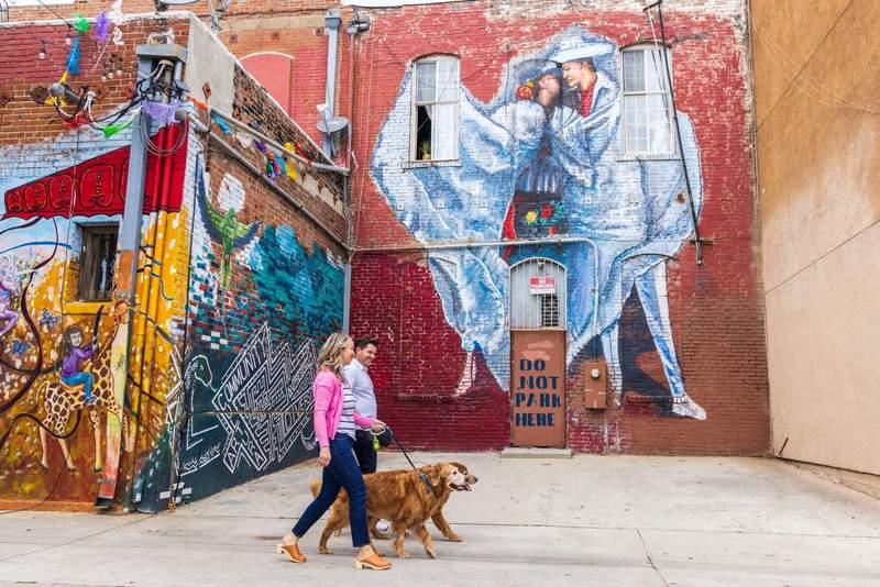 Couple walking their dog past a huge mural of a couple kissing and a sign that says do not park here.