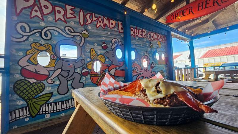 A burger sitting in front of a colorful mural for a restaurant 
