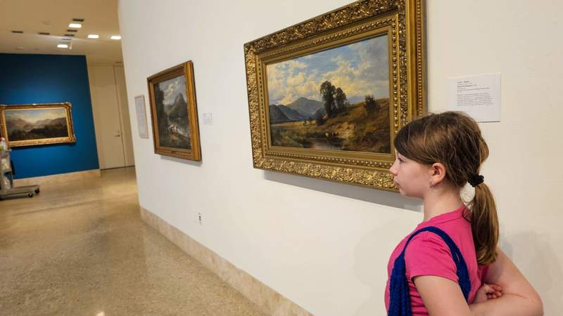 A young girl in pink walking through an art gallery observing the art work on the walls 