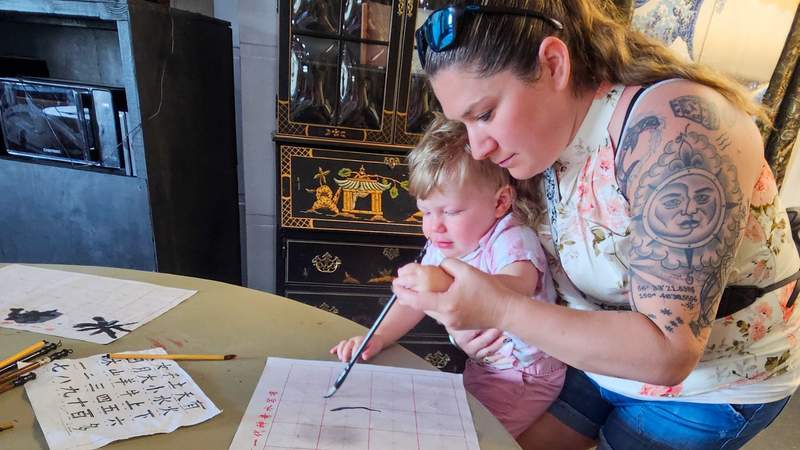 A mother and young boy using the calligraphy paint brushes for Japanese at a museum 