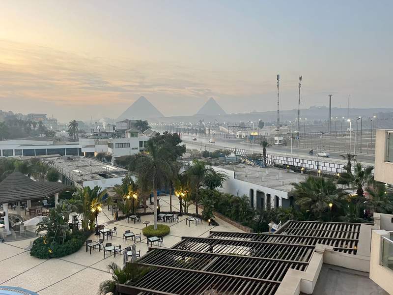 The ancient Pyramids of Giza rising majestically through a soft layer of morning mist from hotel balcony at sunrise.
