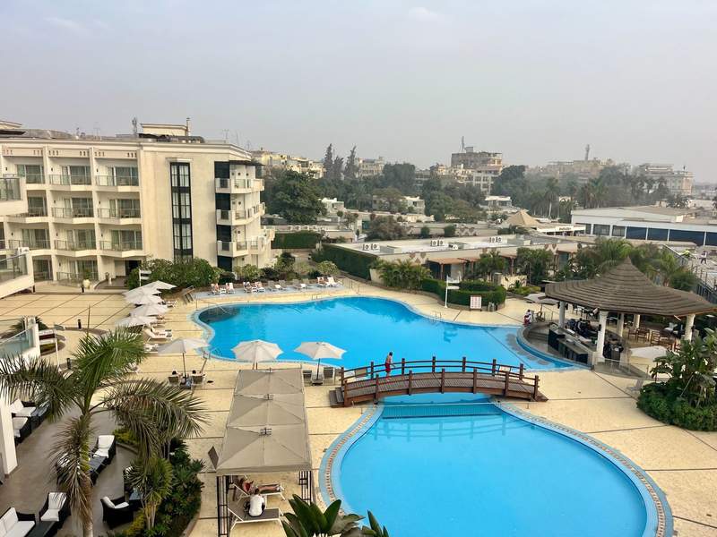 A sparkling clear blue swimming pool at a luxury hotel with the ancient city of Cairo in the background.