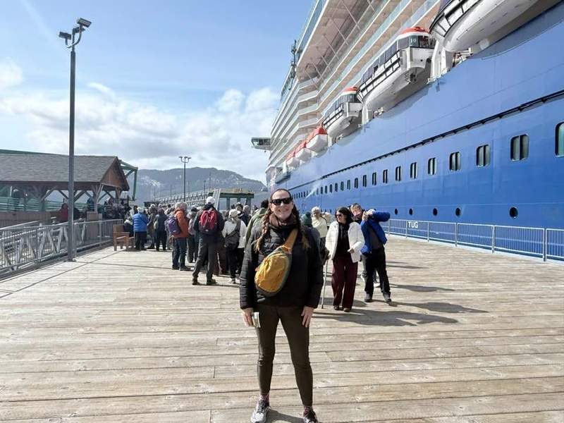 Woman standing on the peer in front of the Celebrity Solstice in Alaska.