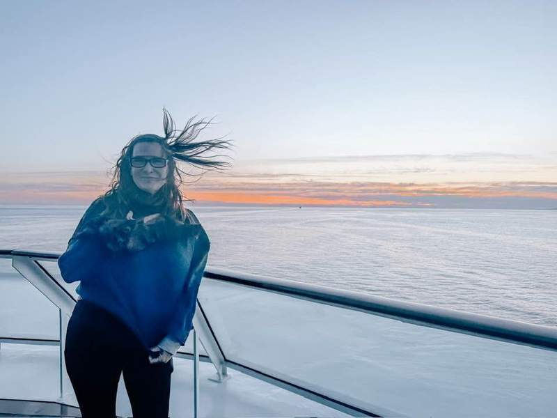 Woman with her hair blowing in the wind and standing on the deck of the Celebrity Solstice in Alaska at sunset.