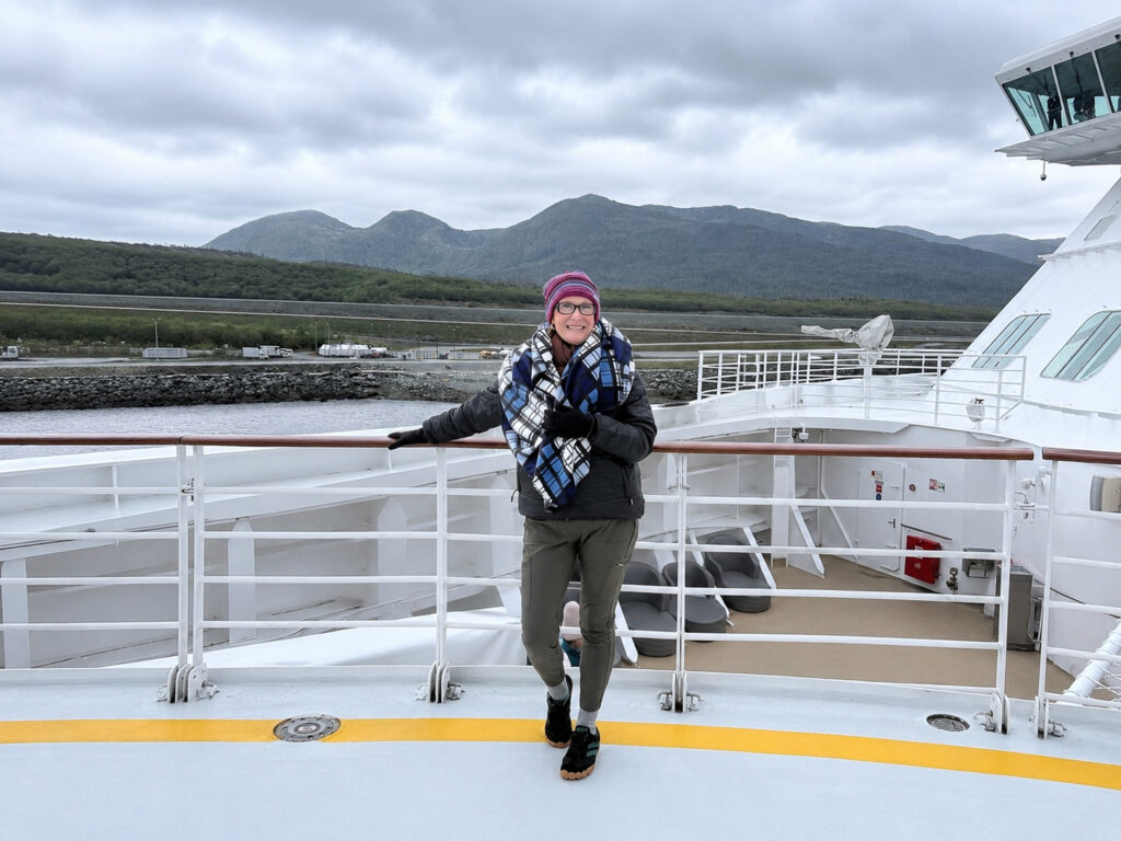 Woman wrapped in warm layers and standing on the deck of the Celebrity Solstice in Alaska
