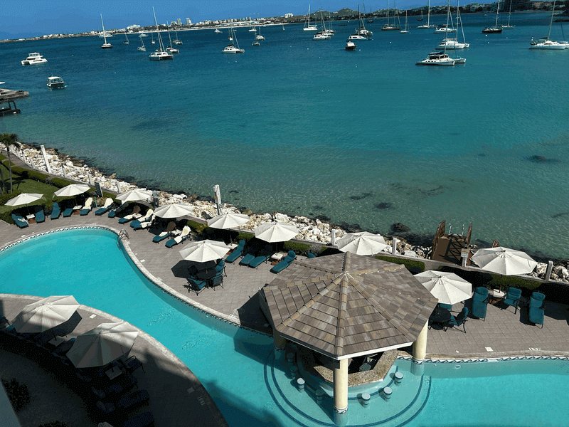 A scenic view of the expansive swimming pool, marina docks, and calm blue waters of Simpson Bay Resort at sunset.