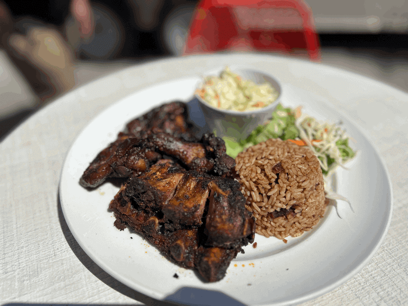 A generous lunch plate from Captain’s Rib Shack featuring a large slab of barbecued ribs, potato salad, rice and beans, and a side salad.