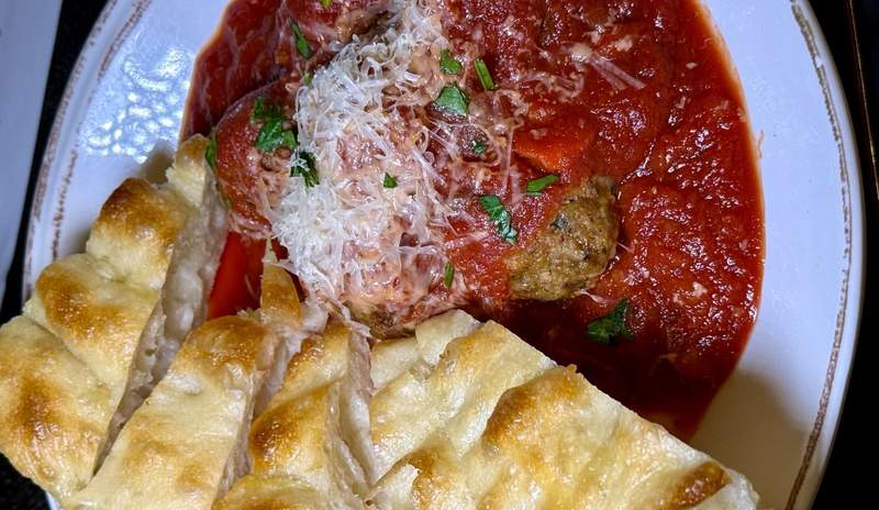 Red tomato sauce with grated parmesan and hints of chopped green pepper fill a round dinner plate. Strips of fresh bread line the bottom third of the plate.