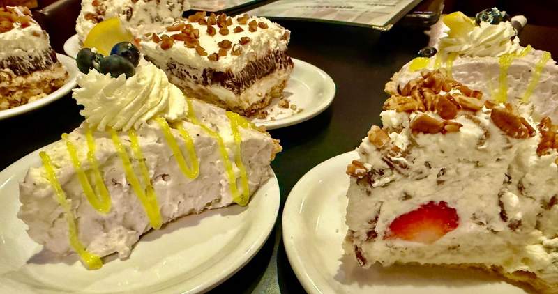 Four slices of pie include whipped cream and blueberries. Some have chopped nuts on top. A strawberry pokes out the  inside of another slice.