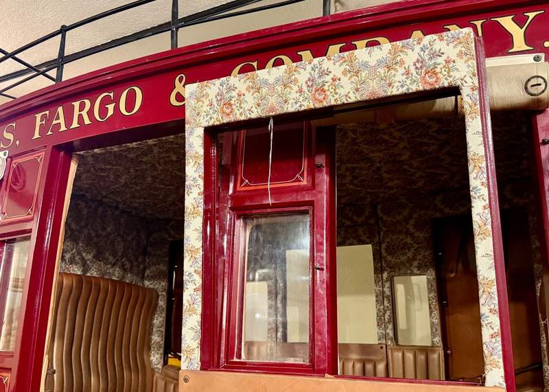 Red paint surrounds the open stagecoach door and flowers fill the fabric framing the window. A bit of the luggage rack on top shows.