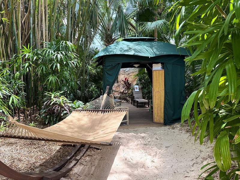 Hammock in front of the green awning of a private cabana with lush foliage surrounding it