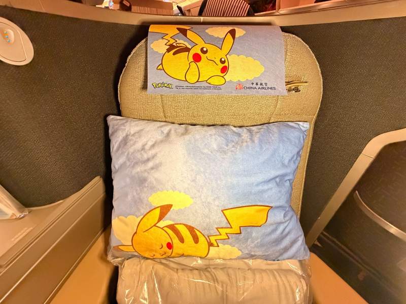 Airline seat with the Pikachu character printed on a felt headrest and a lavender pillow with a bright yellow Pikachu sleeping.