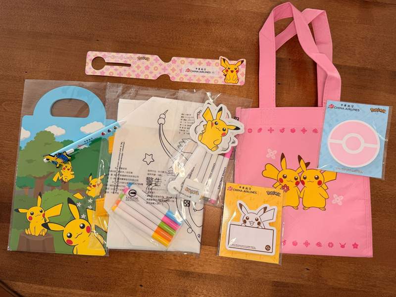 Pikachu cardboard kids' meal box, flat, paper luggage tag, coloring kits, note pads and a pink vinyl bag.
