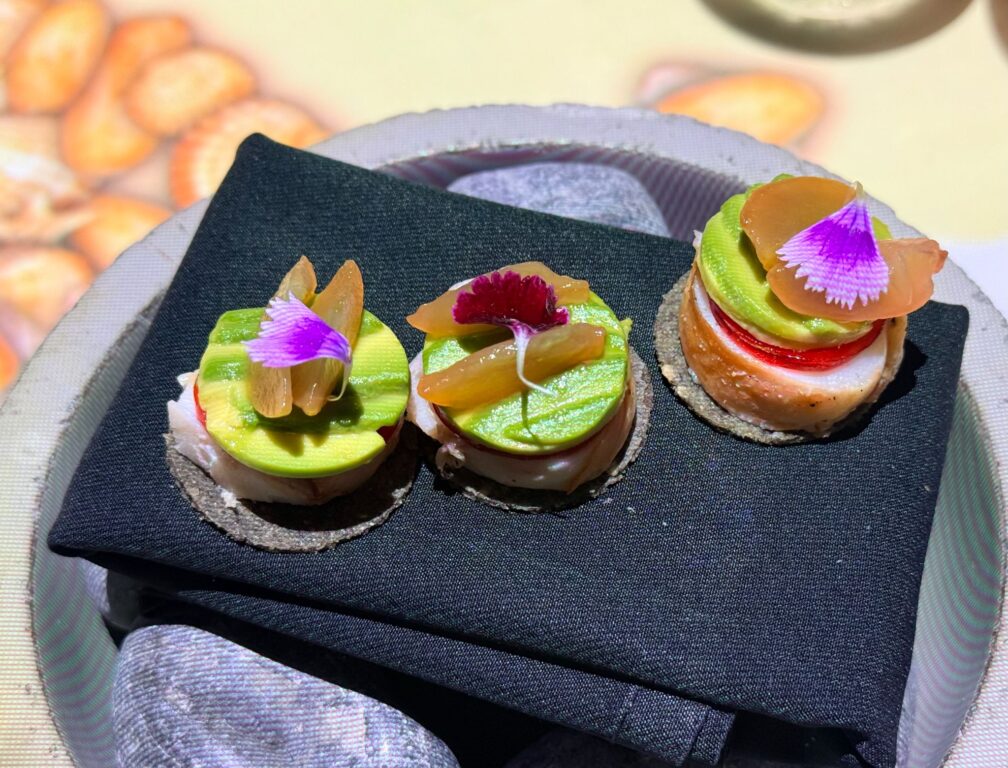 A vibrant trio of gourmet lobster tacos garnished with fresh avocado slices and bright citrus elements on a contemporary plate.