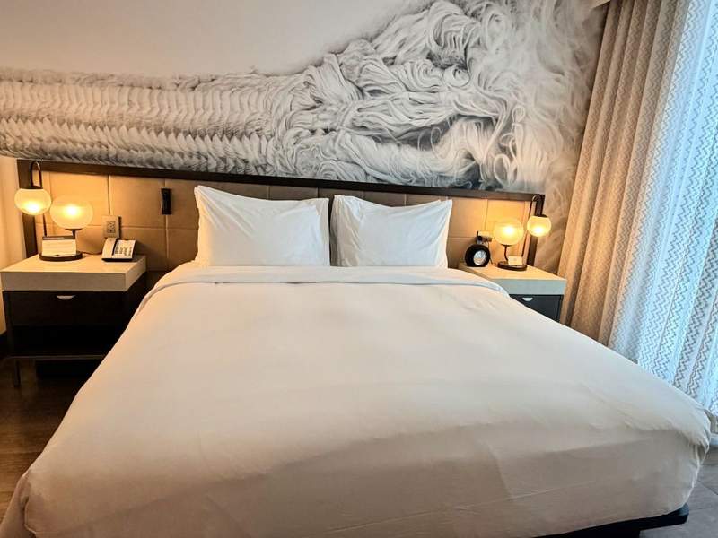 Modern hotel room interior at Hyatt Centric Las Olas featuring crisp white linens, a colorful wall mural and warm ambient lighting.