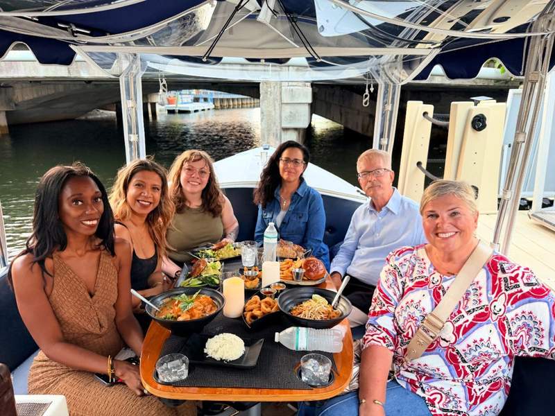 A group of smiling female friends enjoying a sunset gondola dinner cruise along the Fort Lauderdale canals.