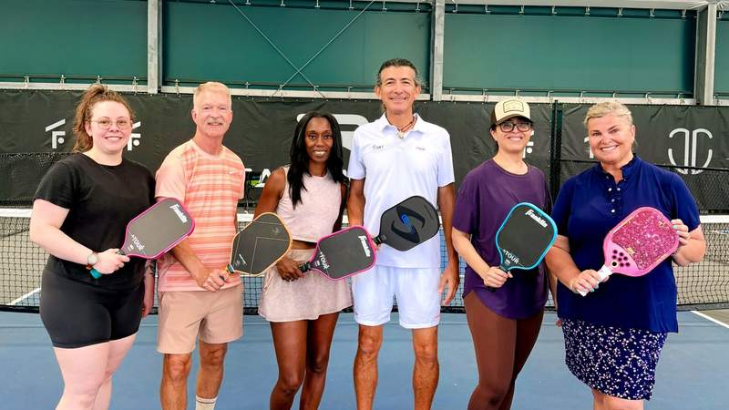 A group of people participating in a pickleball clinic on outdoor courts at The Fort stadium in Fort Lauderdale.