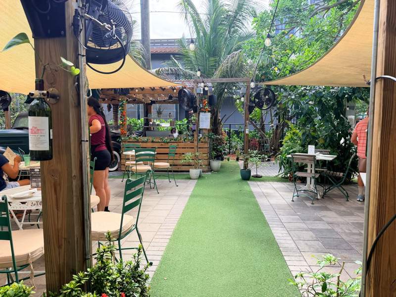 Lush green plants, potted trees and cozy seating inside the indoor-outdoor dining space at Emily's Garden coffee bar.