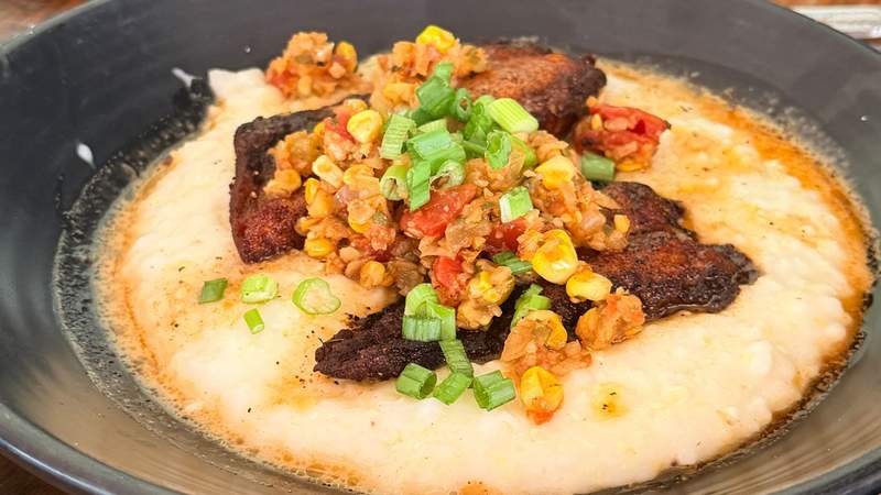 A gourmet plate of Southern-style shrimp and grits with fresh corn, bacon and rich sauce on a restaurant table.