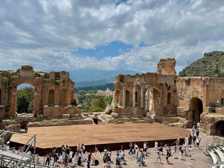 Ancient stone ruins of a 3rd-century Greco-Roman theater in Taormina, featuring weathered brick arches and columns overlooking a beautiful mountainside.
