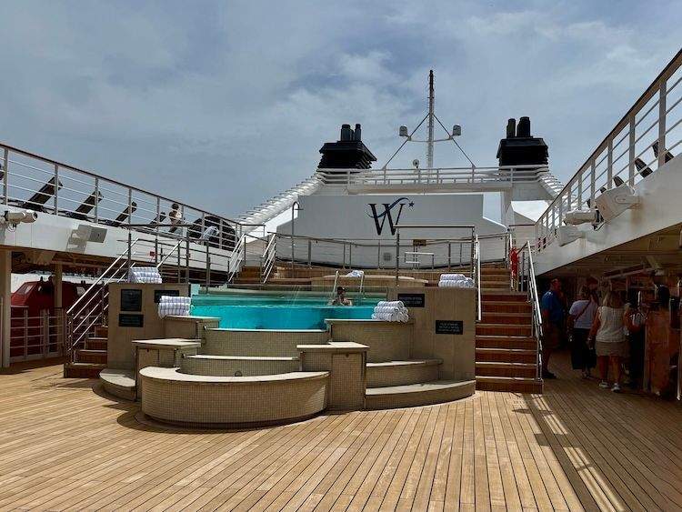 A sleek, modern infinity pool and elevated whirlpool on the Star Legend cruise ship, surrounded by warm teak lounge decks under a bright sky.