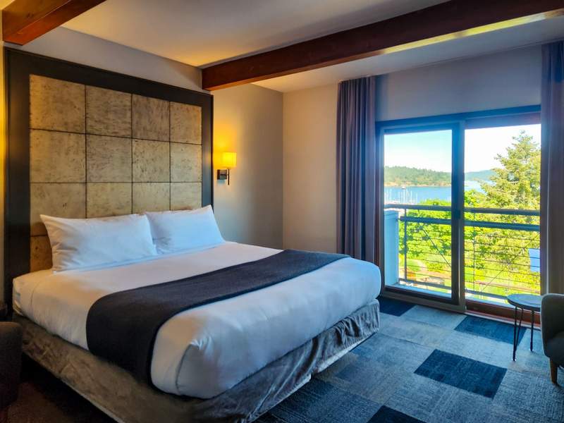 A cozy, upscale guest room at Friday Harbor House featuring a king-sized bed, a warm fireplace, and a large jetted tub for two, with windows looking out toward the marina.