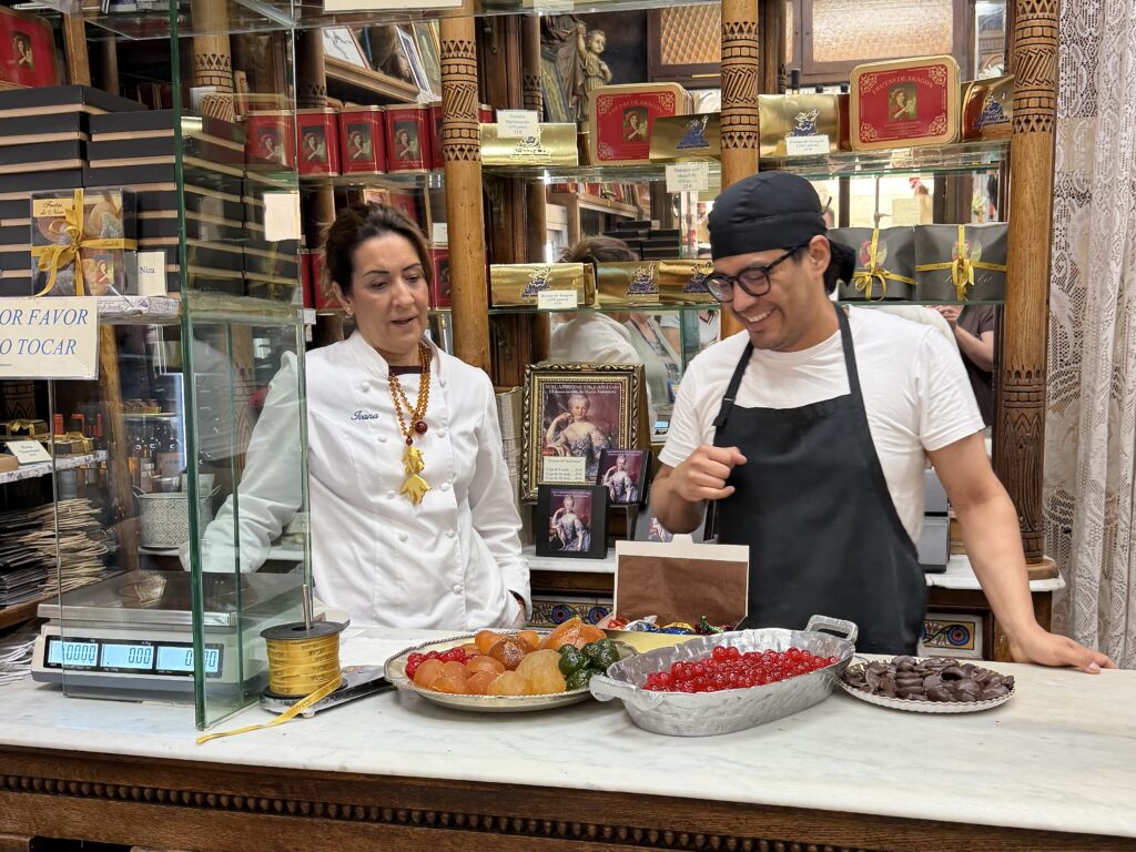 Woman and man in candy shop with counter full of candied fruits and chocolate in Zaragoza Spain