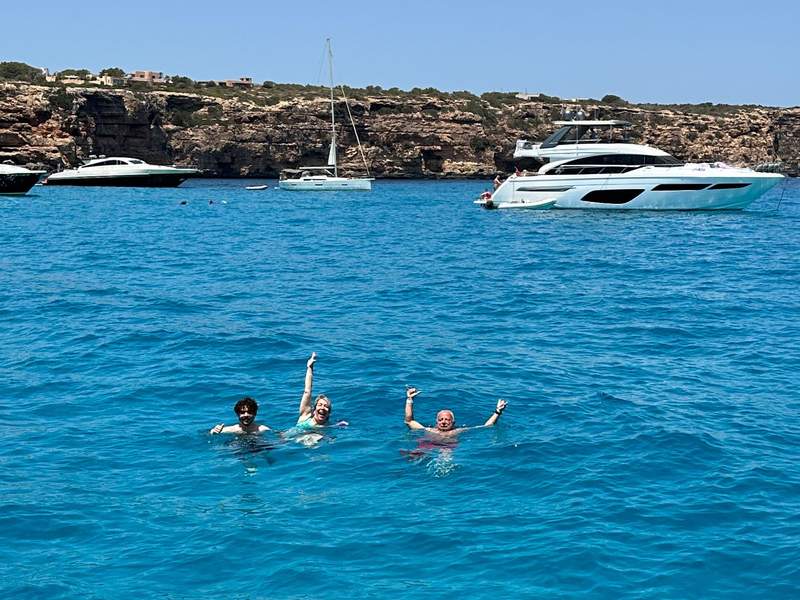 Author’s family swimming in turquoise waters with various yachts in the background.