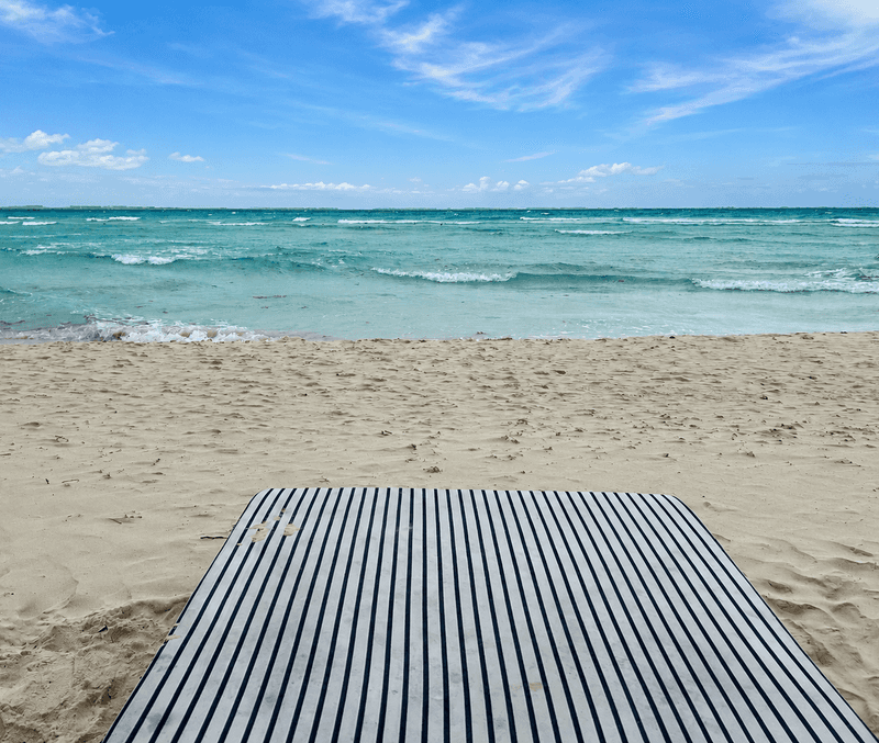 A striped beach mat lies on white sand looking out at the turquoise Caribbean Sea on Playa Norte, Isla Mujeres most popular beach.