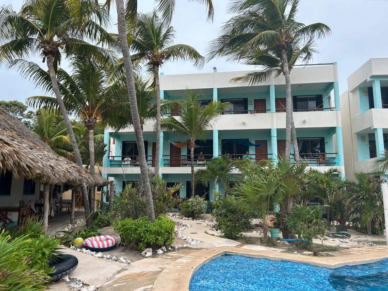 The three-story Hotel Villa Kiin on Isla Mujeres is surrounded by palm trees and lush landscaping, with a curving swimming pool in the foreground.