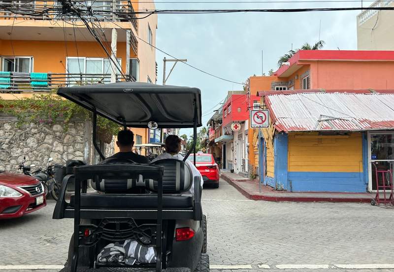 A couple rides a golf cart through the colorful streets of Isla Mujeres.