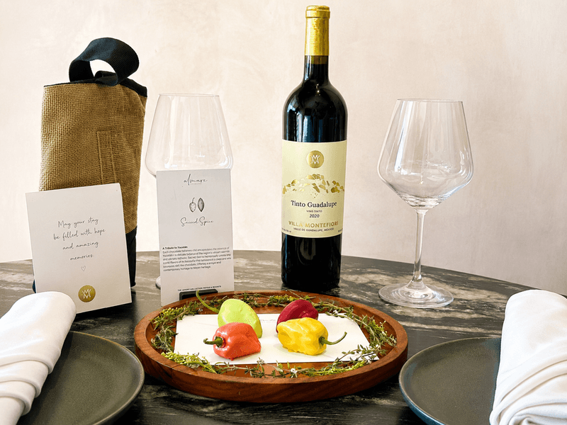 Welcome amenity at Almare Isla Mujeres featuring bottle of Mexican red wine wine glasses, and tray with pepper shaped chocolates.