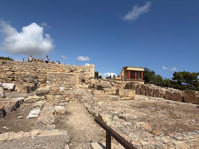 The stone ruins of Knossos Palace can be seen in this wide view of the UNESCO complex. Stone walls and the remains of the palace's foundations are visible.