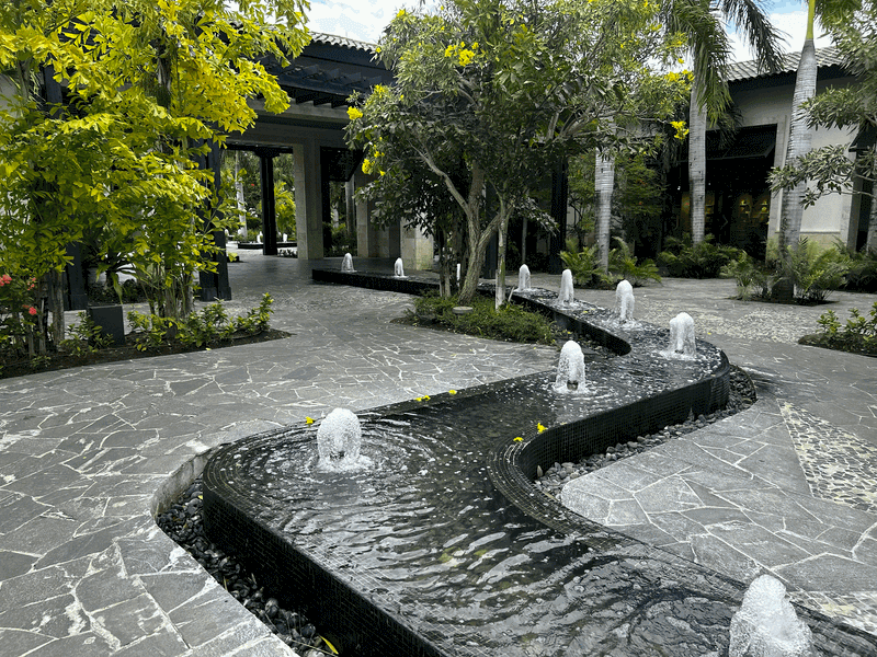 Winding stone pathways surrounded by lush tropical landscaping and clear, bubbling ponds at a luxury resort.